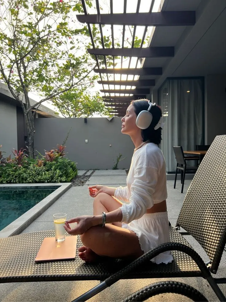 Woman meditating poolside with headphones at sunrise